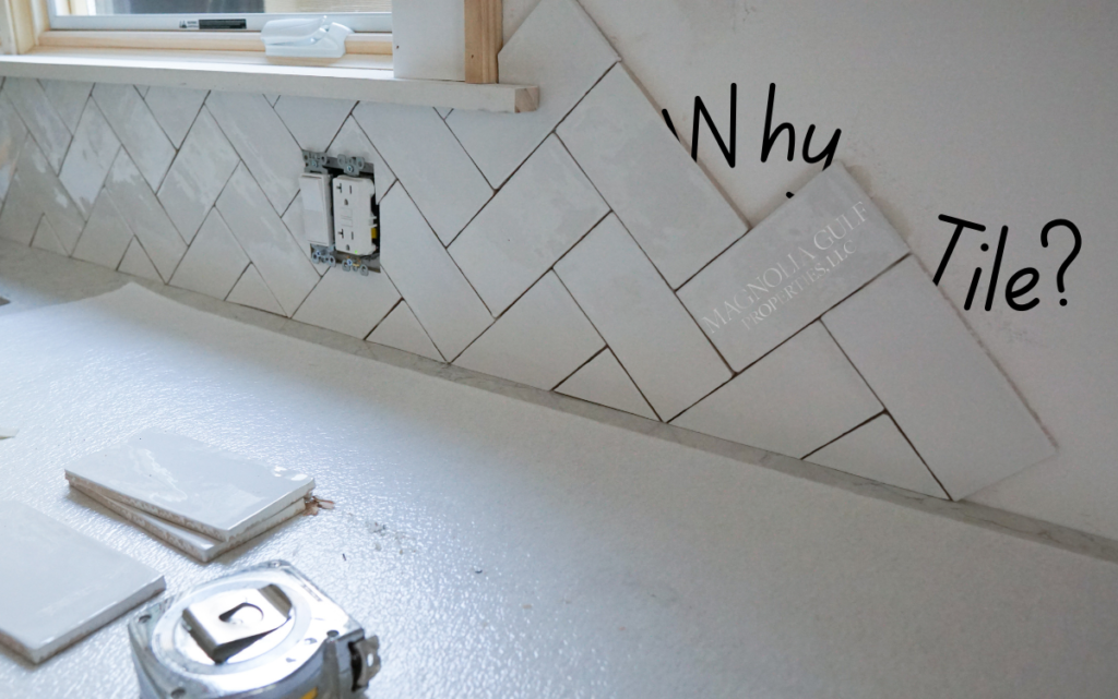 White subway tile backsplash being installed in a herringbone pattern, with an electrical outlet cutout and loose tiles on the countertop.
